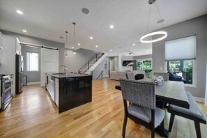 A modern kitchen with a central island, a dining area with a table and chairs, and a staircase leading to an upper level.