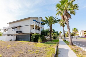 Un edificio residencial de dos pisos con balcón, rodeado de palmeras y una acera.