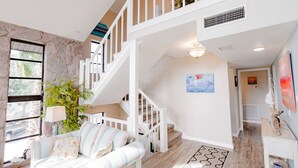 Un amplio salón con escalera, un sofá, una lámpara y un cuadro en la pared.