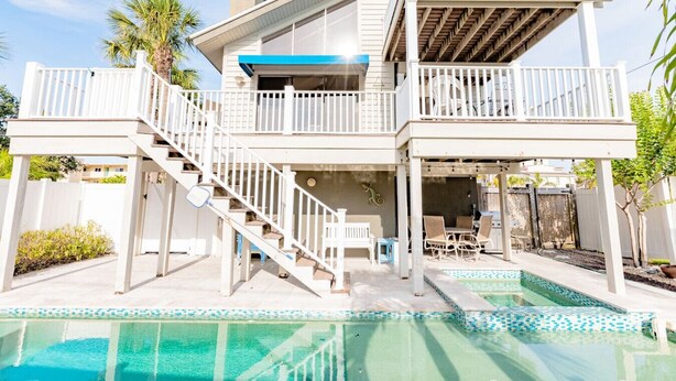 Una casa de dos pisos con piscina, un porche cubierto y una escalera que lleva al nivel superior.