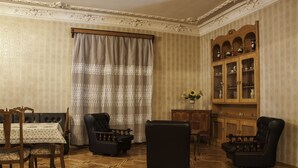 Una stanza con pavimento decorato, un tavolo da pranzo con sedie, due divani, un mobile con ante in vetro e una finestra con tende.