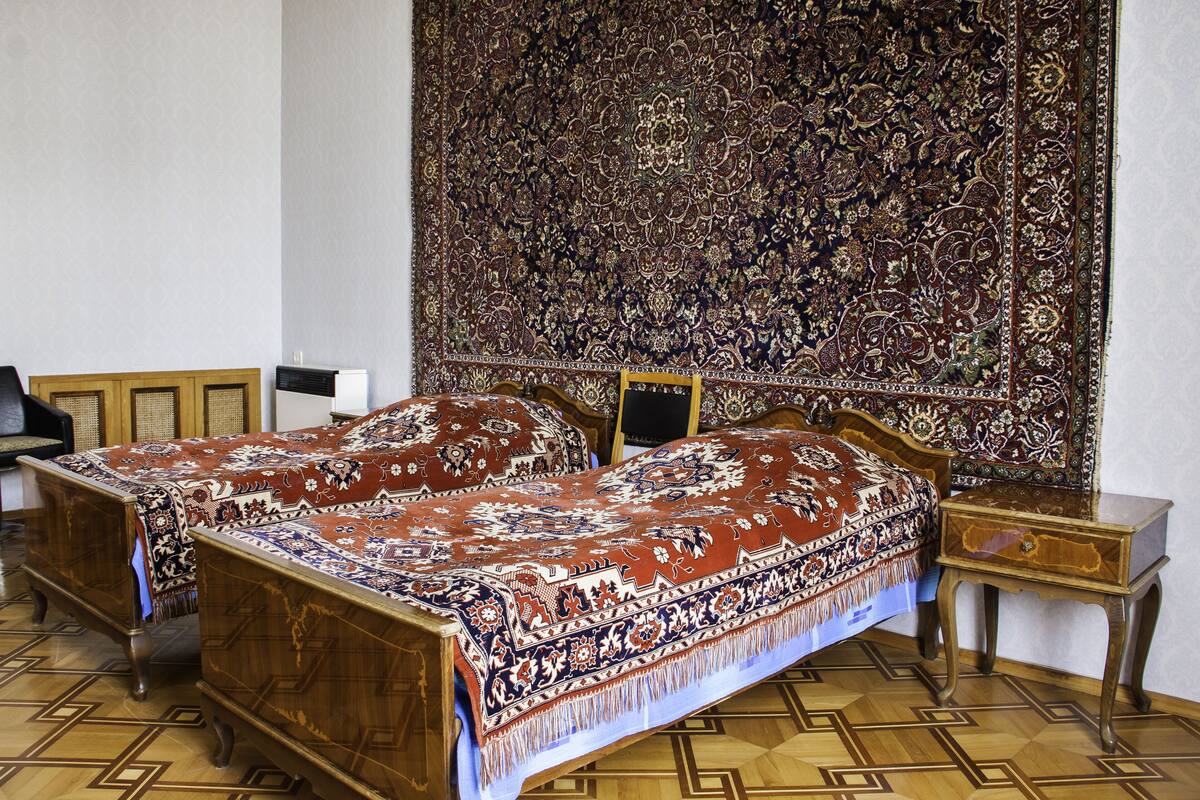 A traditional room with two wooden beds, a large ornate tapestry on the wall, and a small wooden nightstand.
