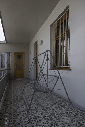 A corridor with patterned floor tiles, a wooden door, a window with metal bars, and a metal swing gate. - Guest House Asmati (Telavi)