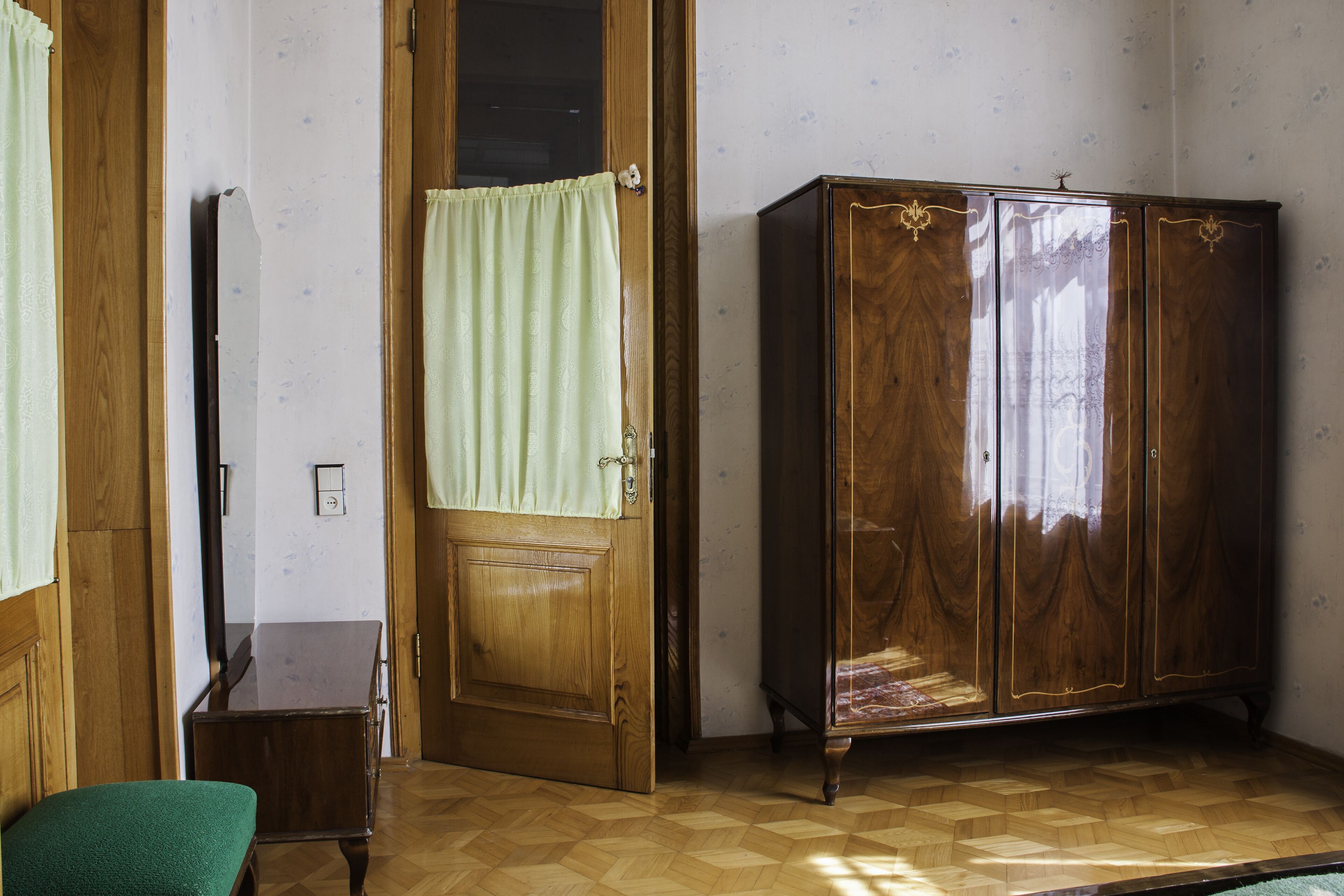 Una habitación con un armario de madera, una silla verde y una puerta de madera con cortina.