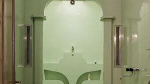 Un bagno con una parete rivestita in piastrelle verdi, un lavandino bianco e una doccia.