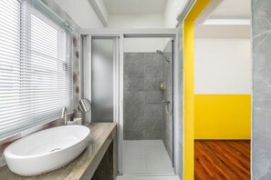 A bathroom with a white sink, a glass shower enclosure, and a yellow accent wall. - The Ram Hotel  (Bangkok)