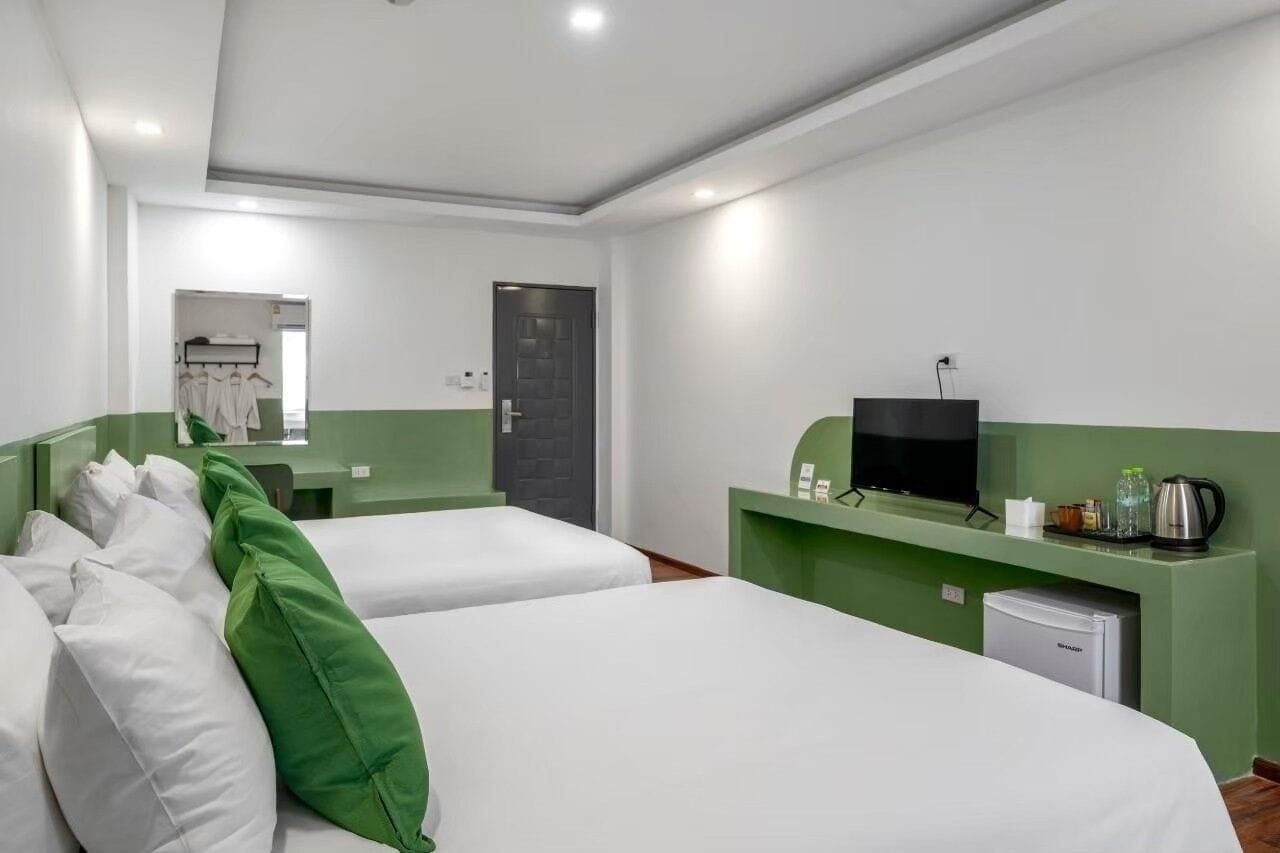 A hotel room with two beds, a television, a small refrigerator, and a mirror.