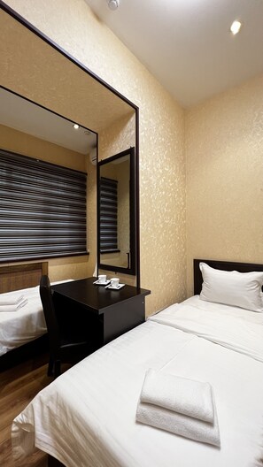A hotel room with a bed, a desk, a chair, a large mirror, and a window with blinds. - Hayot hostel (Tashkent)