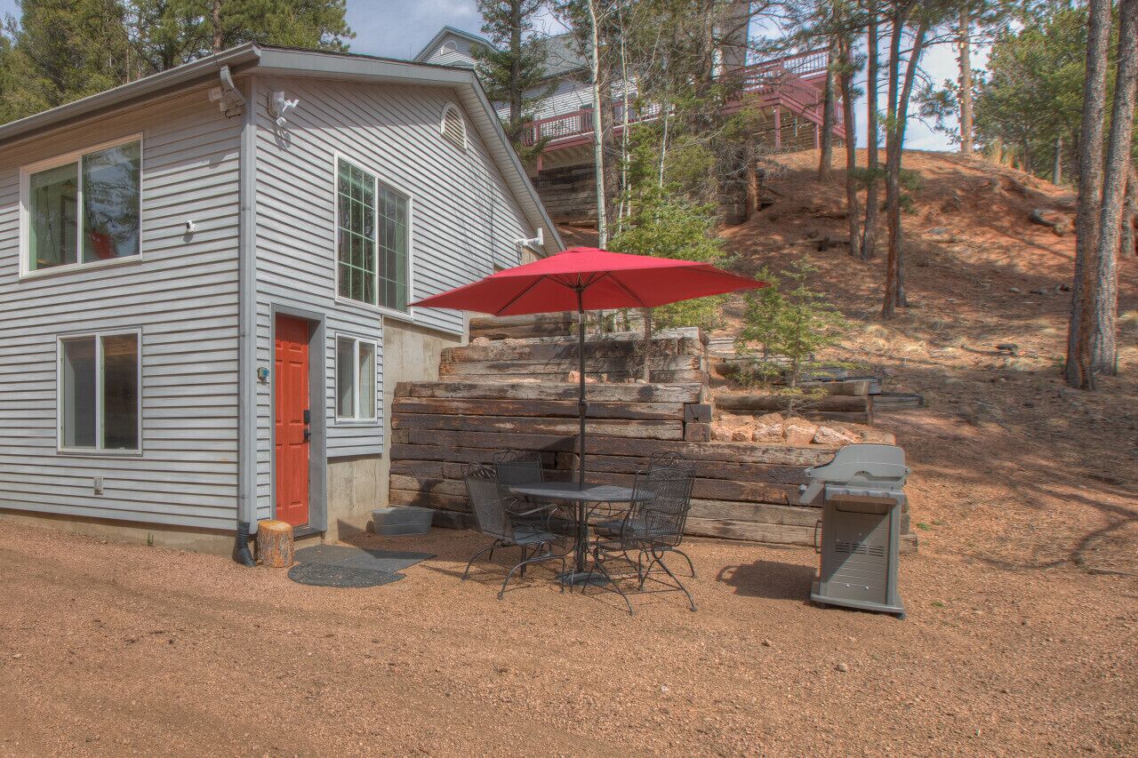 Eine Hütte mit roter Tür, einer Terrasse mit Tisch und Stühlen sowie einem roten Sonnenschirm.