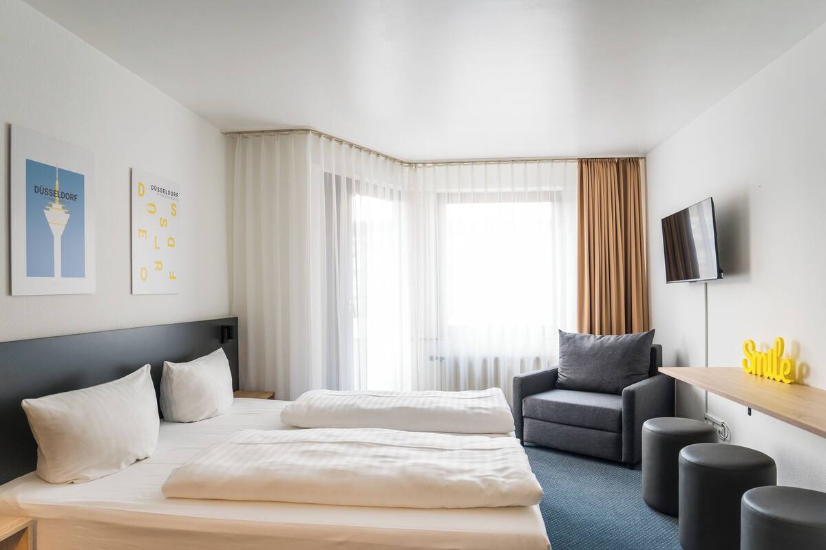 A hotel room with a bed, a desk, a chair, and a TV.