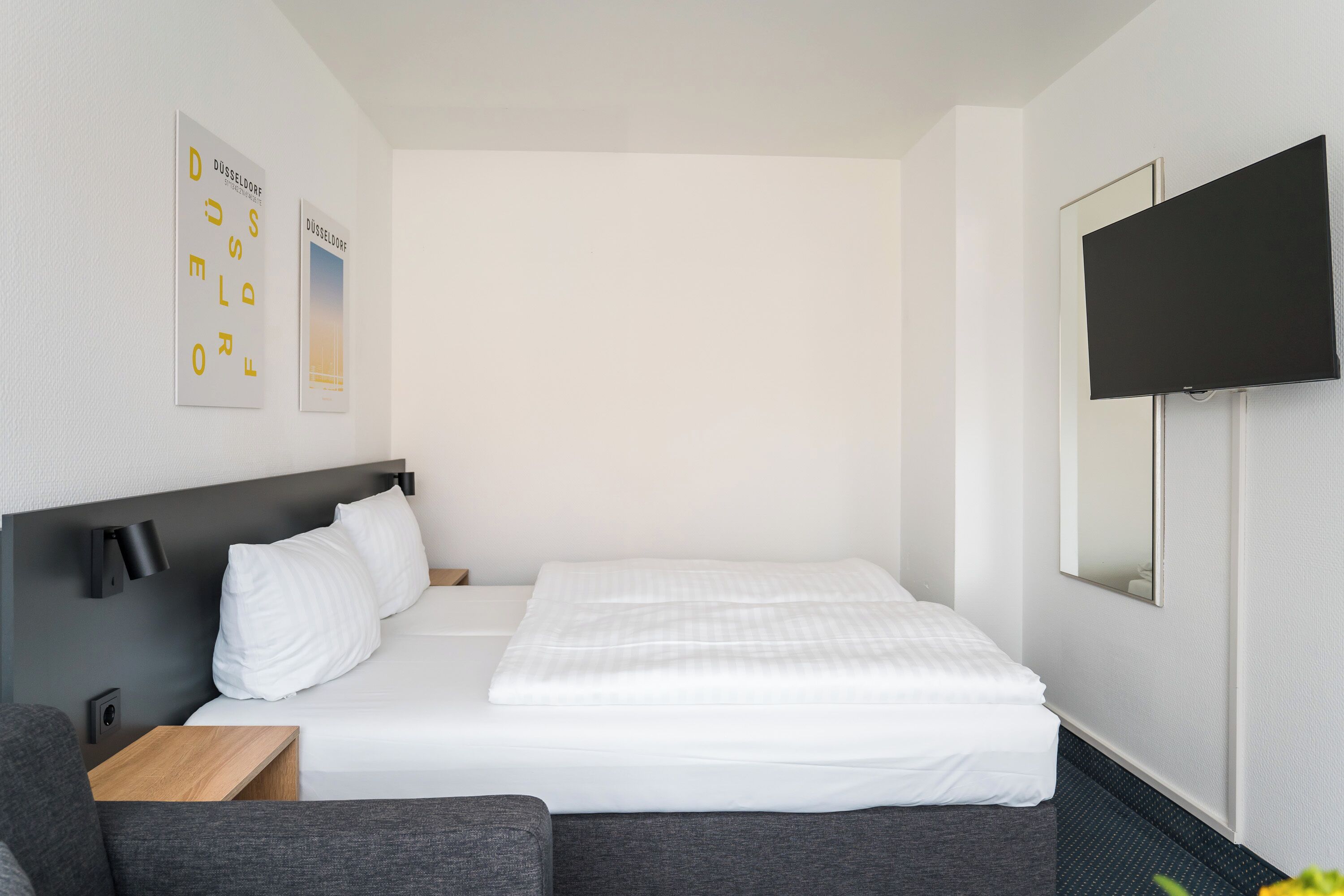 A hotel room with a bed, a TV mounted on the wall, and a small table.