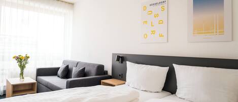 Une chambre d’hôtel avec un lit, un canapé, une table de chevet et un mur orné d’une affiche.