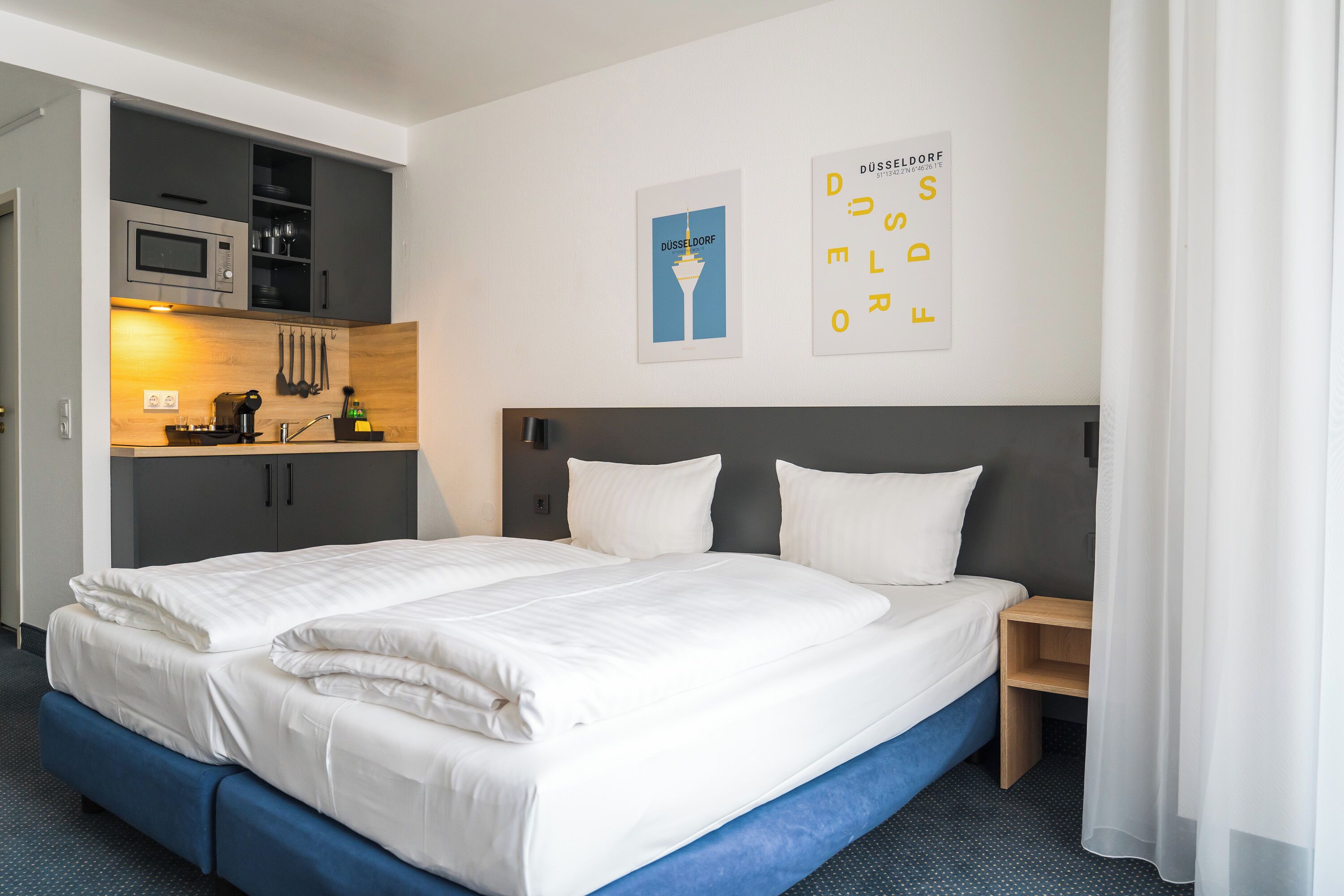 A hotel room with a double bed, a small kitchenette, and a wall-mounted poster.