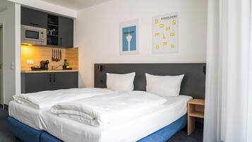 A hotel room with a double bed, a small kitchenette, and a wall-mounted poster.