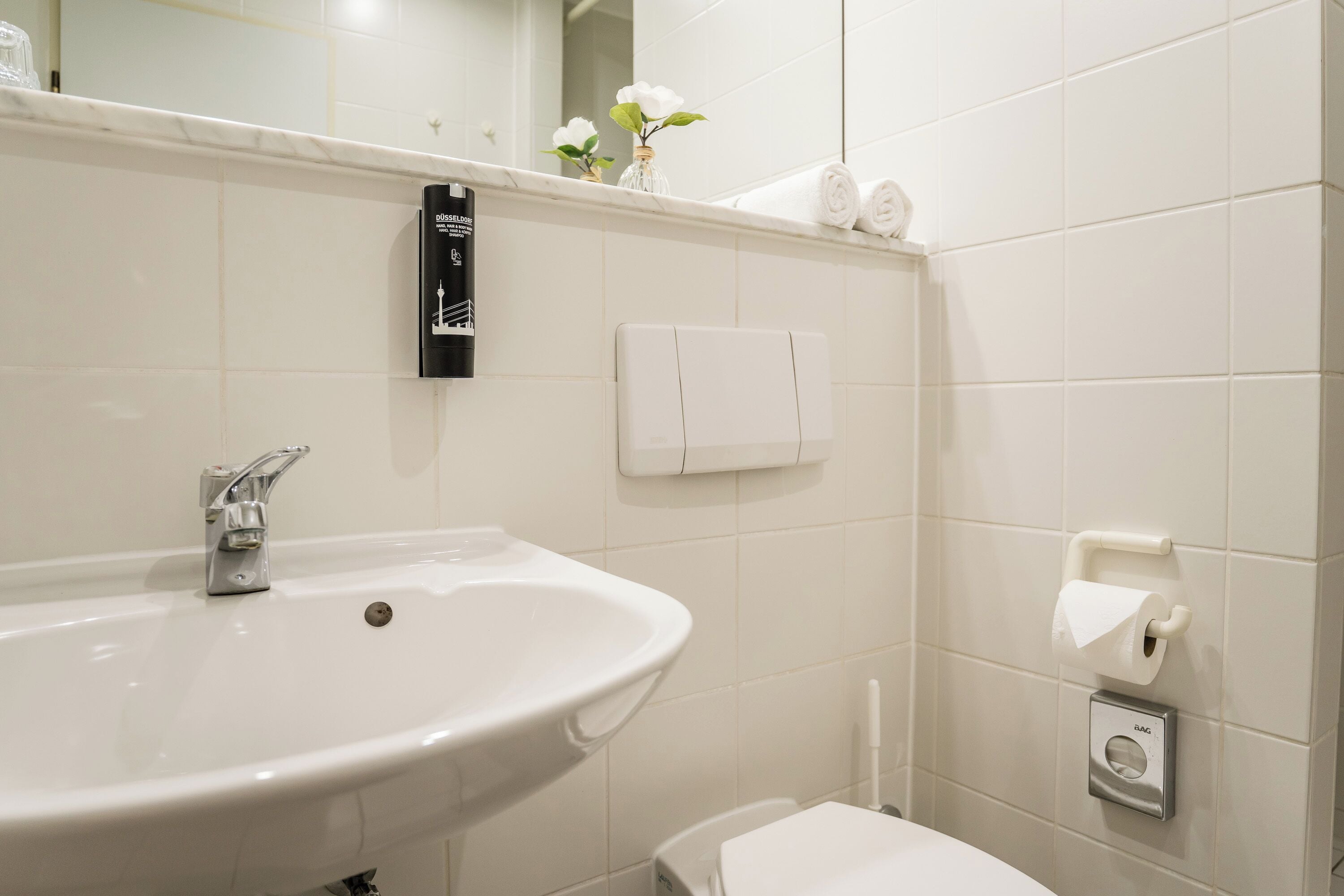 A bathroom with a white sink, a toilet, and a towel dispenser.