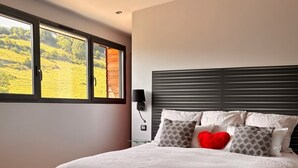 Een moderne slaapkamer met een groot bed, een nachtkastje, een lamp en twee glazen rode drank op een tafel.