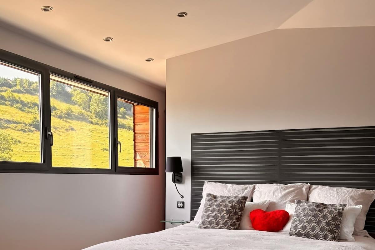 A modern bedroom with a large bed, a nightstand, a lamp, and two glasses of red beverage on a table.