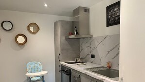 Een compacte keuken met een ingebouwde oven, een spoelbak en een roestvrijstalen afzuigkap. Er staat een kinderstoel en er hangt een decoratieve spiegel aan de muur.