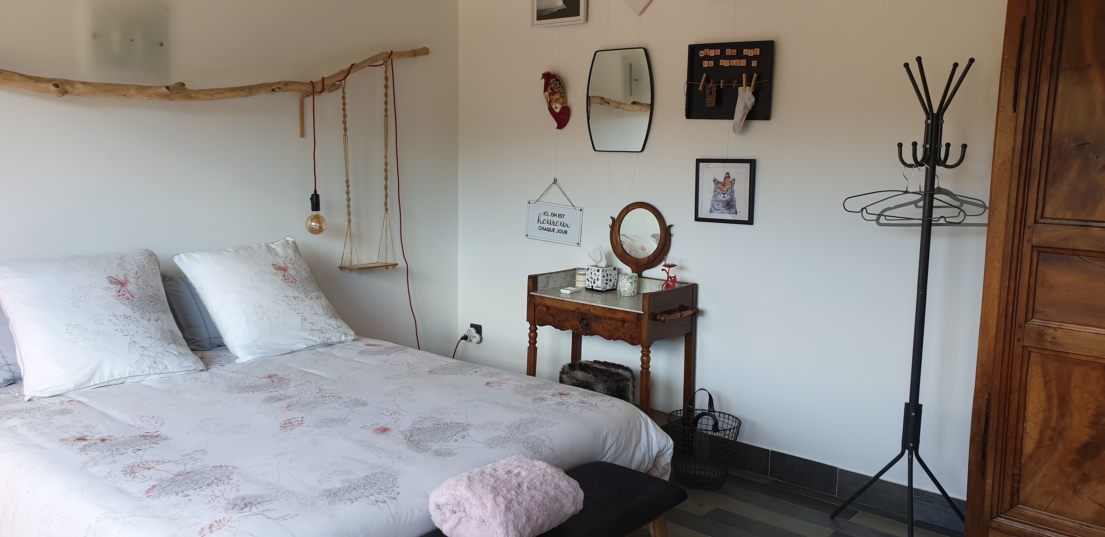 A bedroom with a bed, a wooden dresser, a mirror, and a coat rack.