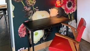 Een kamer met een wanddecoratie van grote bloemen, een kleine tafel met een lamp en een rode stoel.