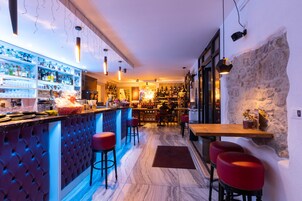 A bar area with a marble floor, red bar stools, and a variety of bottles and glasses on shelves.