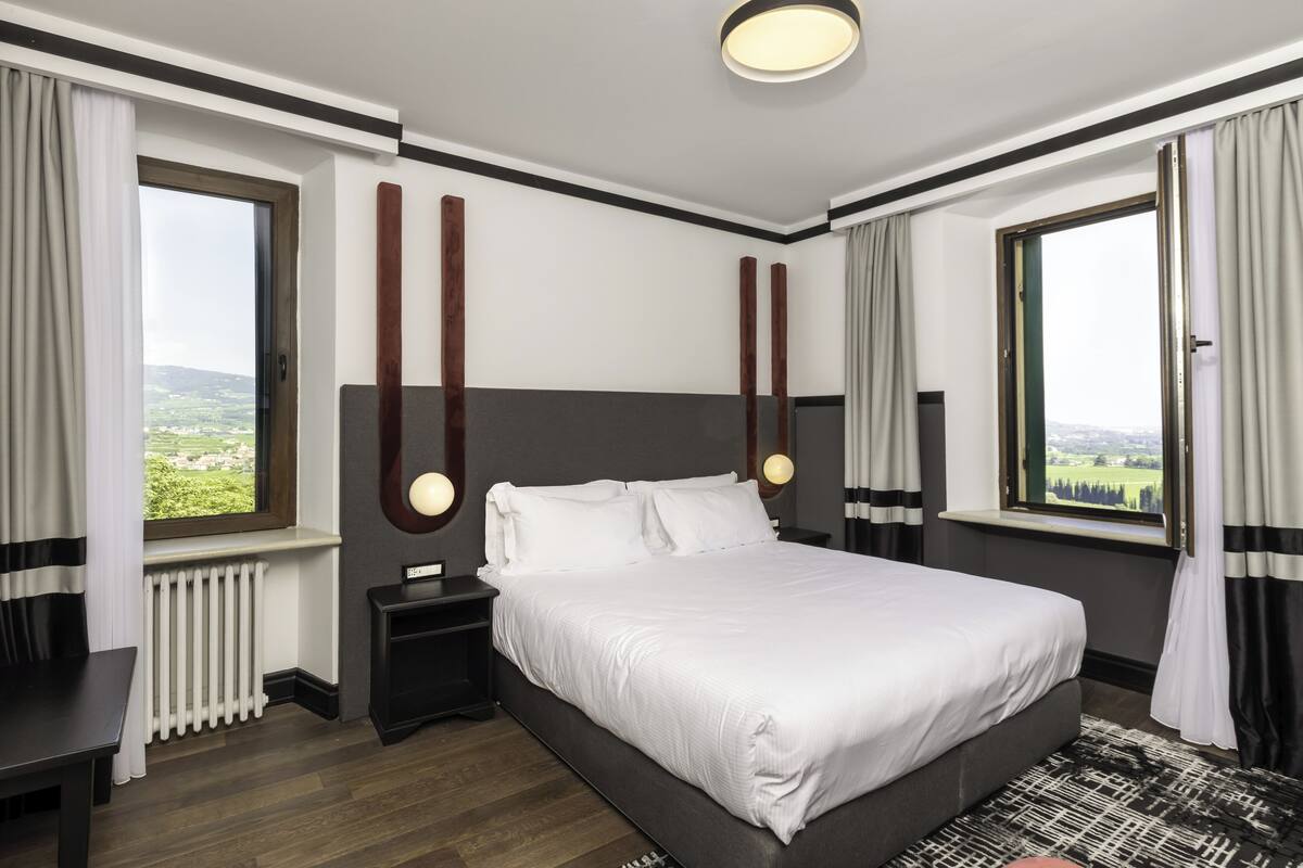 A hotel room with a large bed, a nightstand, a window with a view, and a ceiling light.