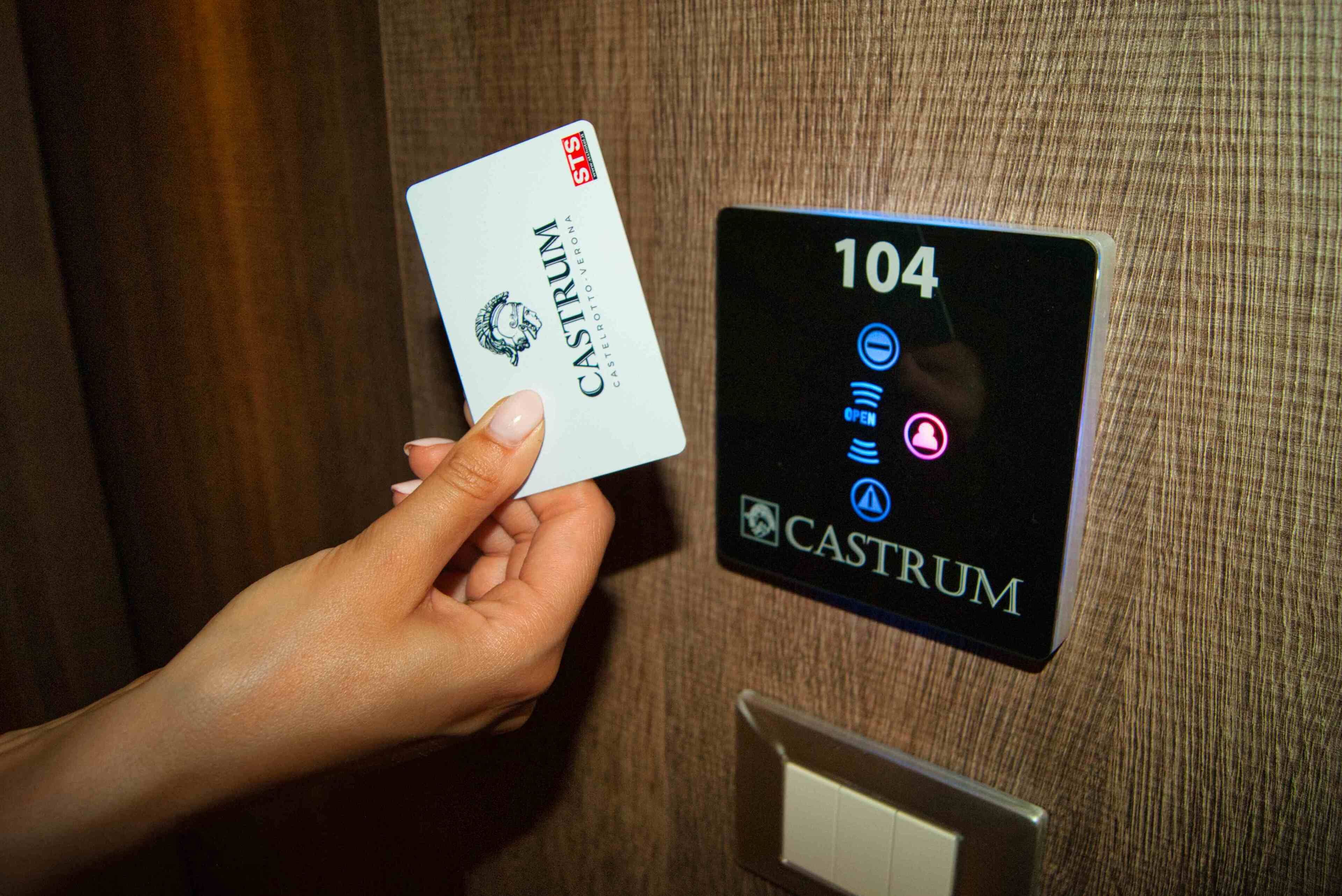 A hand holding a card labeled "CASTRUM" near a digital elevator panel displaying the number "104".