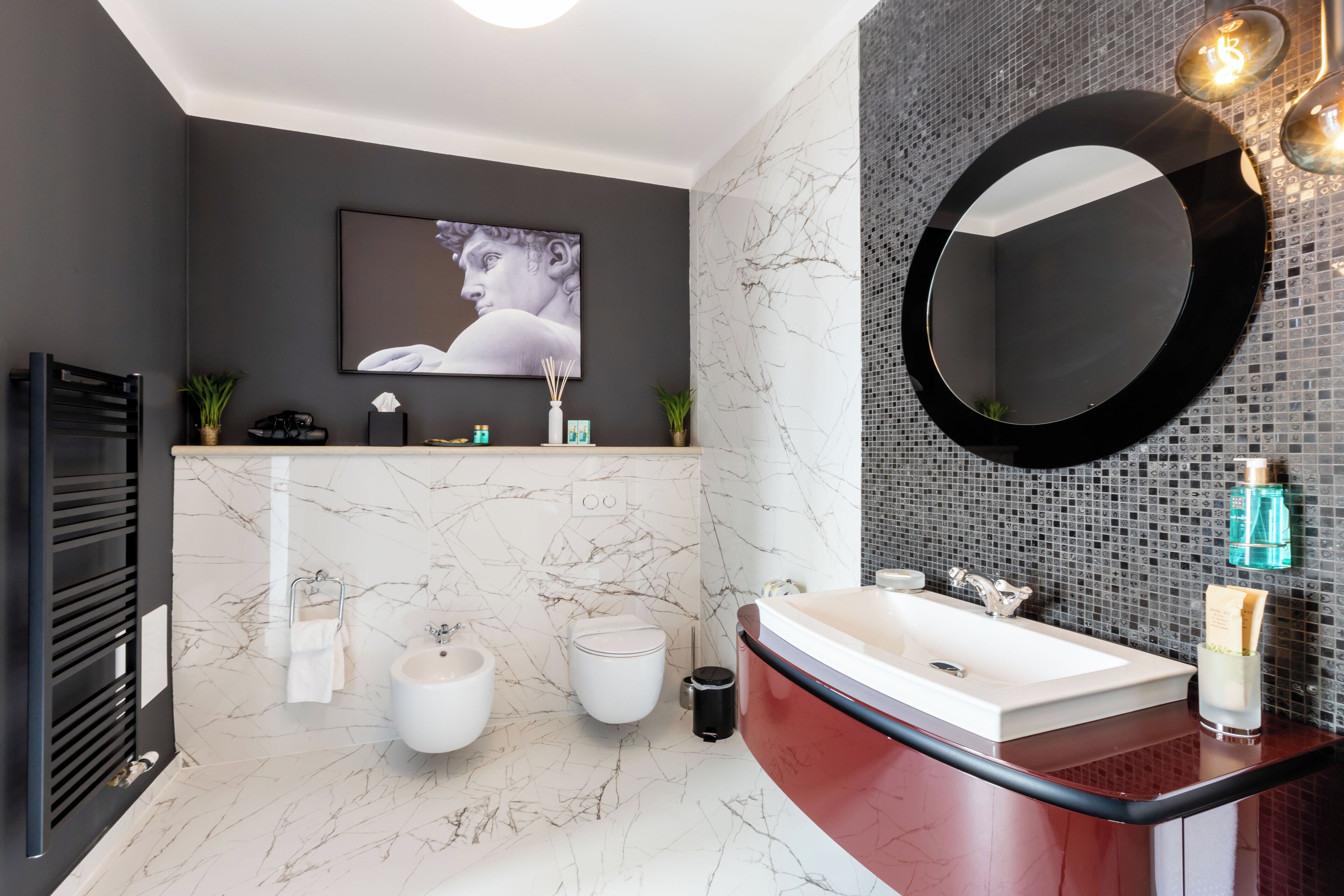 Ein modernes Badezimmer mit Marmorboden, einem schwarzen Waschtisch, einem großen Spiegel und einem an der Wand montierten Fernseher.