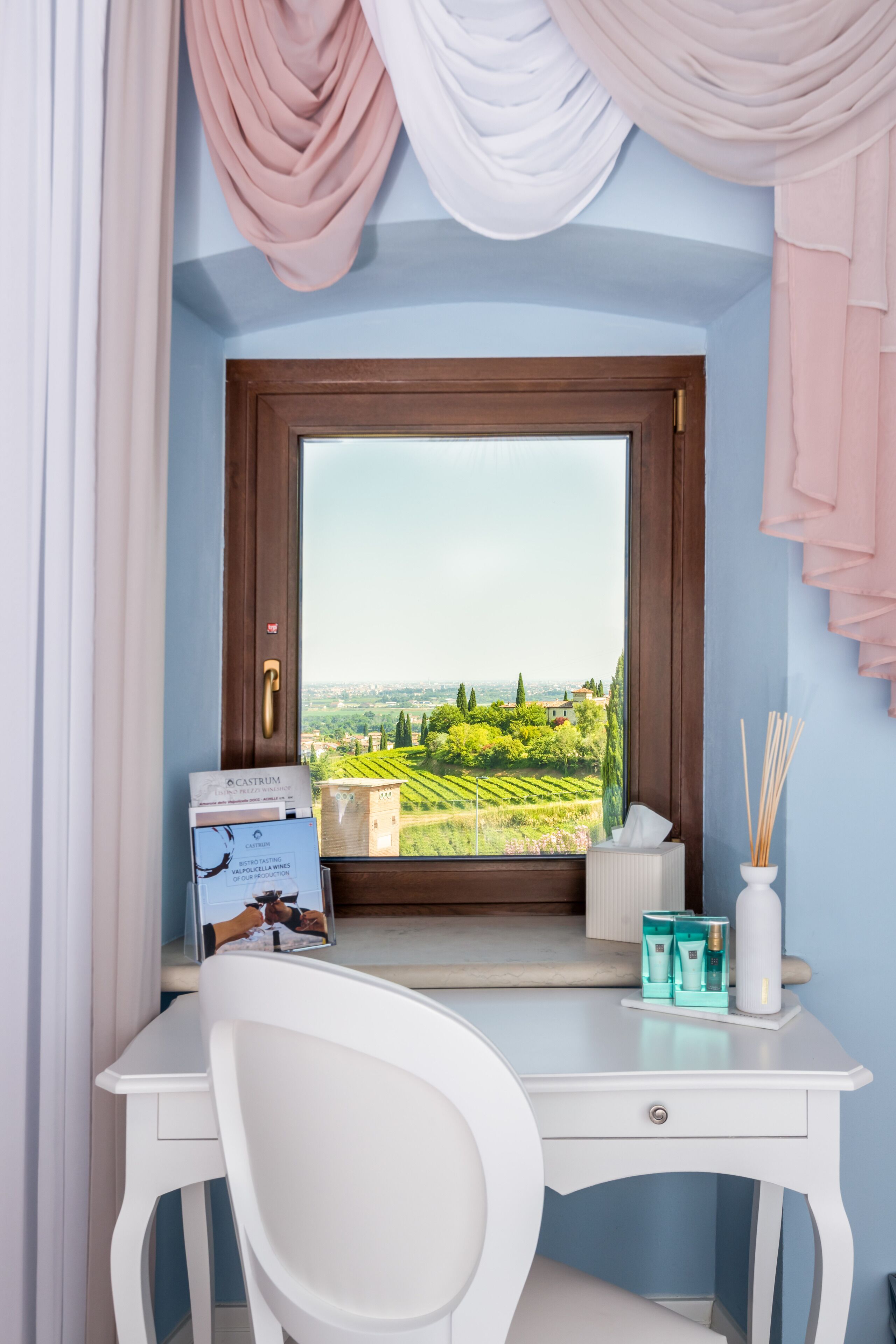 Ein Zimmer mit Schreibtisch, Stuhl, Fenster und Blick auf Weinberge sowie einer Tür mit Griff.