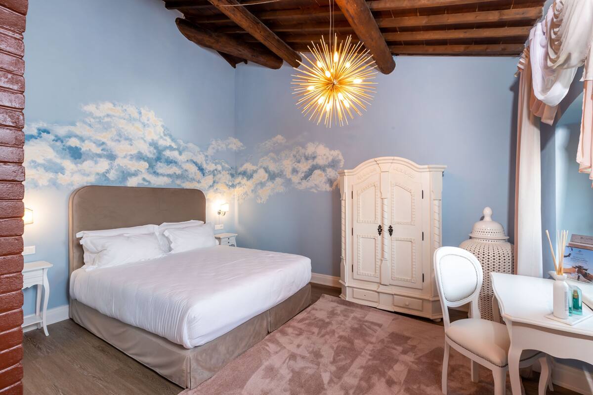 A bedroom with a bed, a white wardrobe, a desk with a chair, and a decorative ceiling light.
