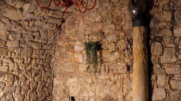 A rustic dining area with stone walls, a wooden table, red upholstered chairs, and a chandelier.