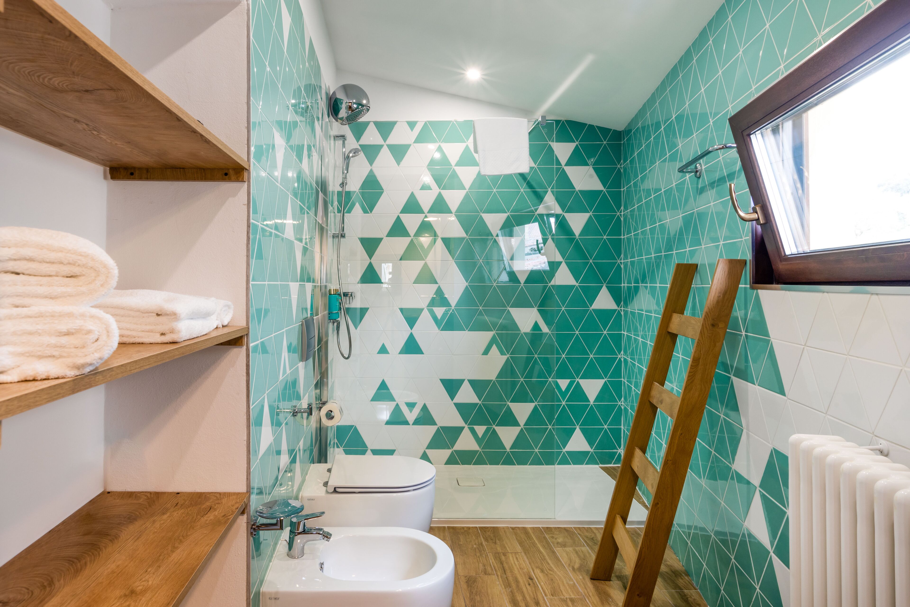 A bathroom with a toilet, bidet, and a wooden shelf with towels.