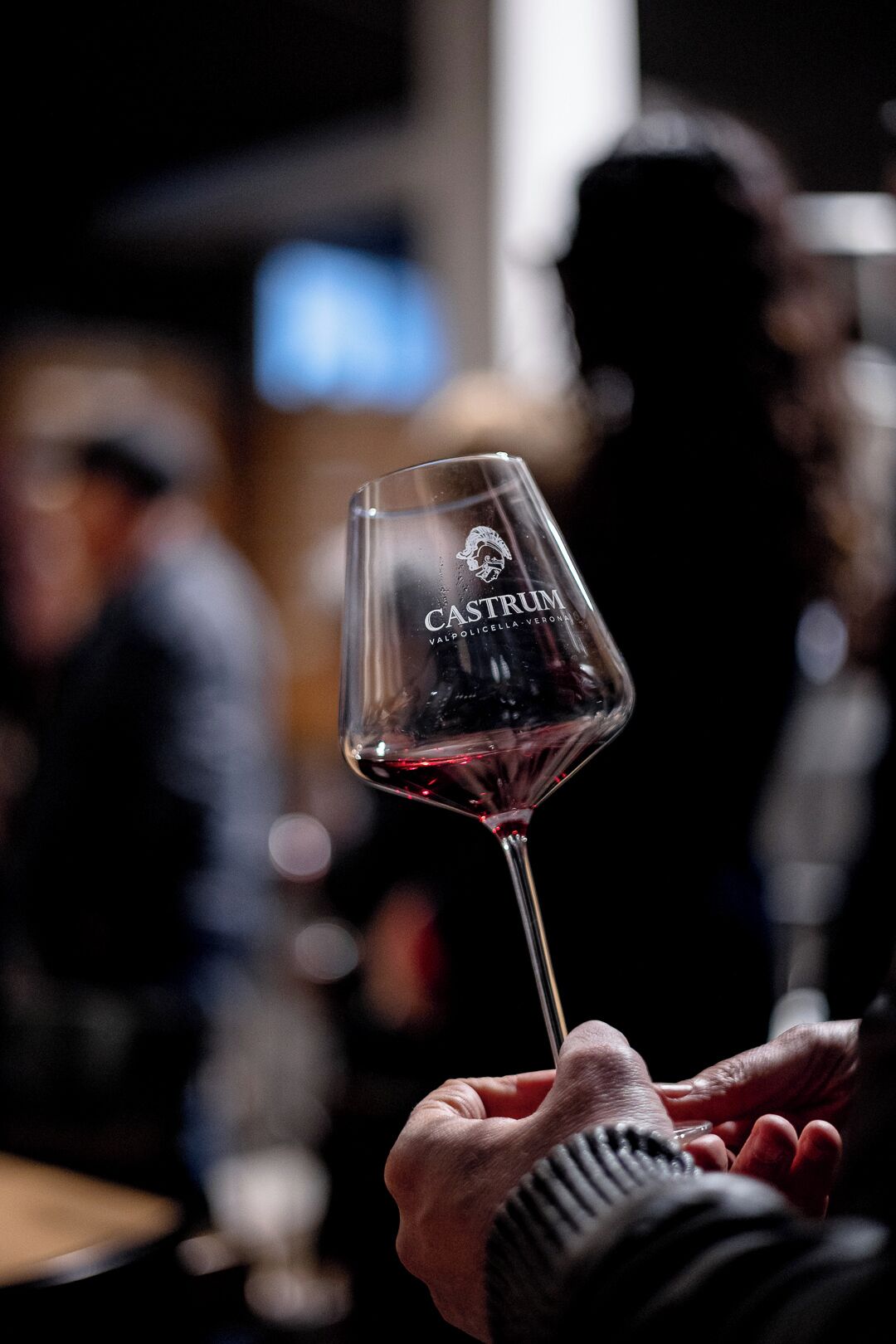 Eine Nahaufnahme einer Hand, die ein Weinglas mit der Aufschrift "CASTRUM VALPOLICELLA VERONA" hält.