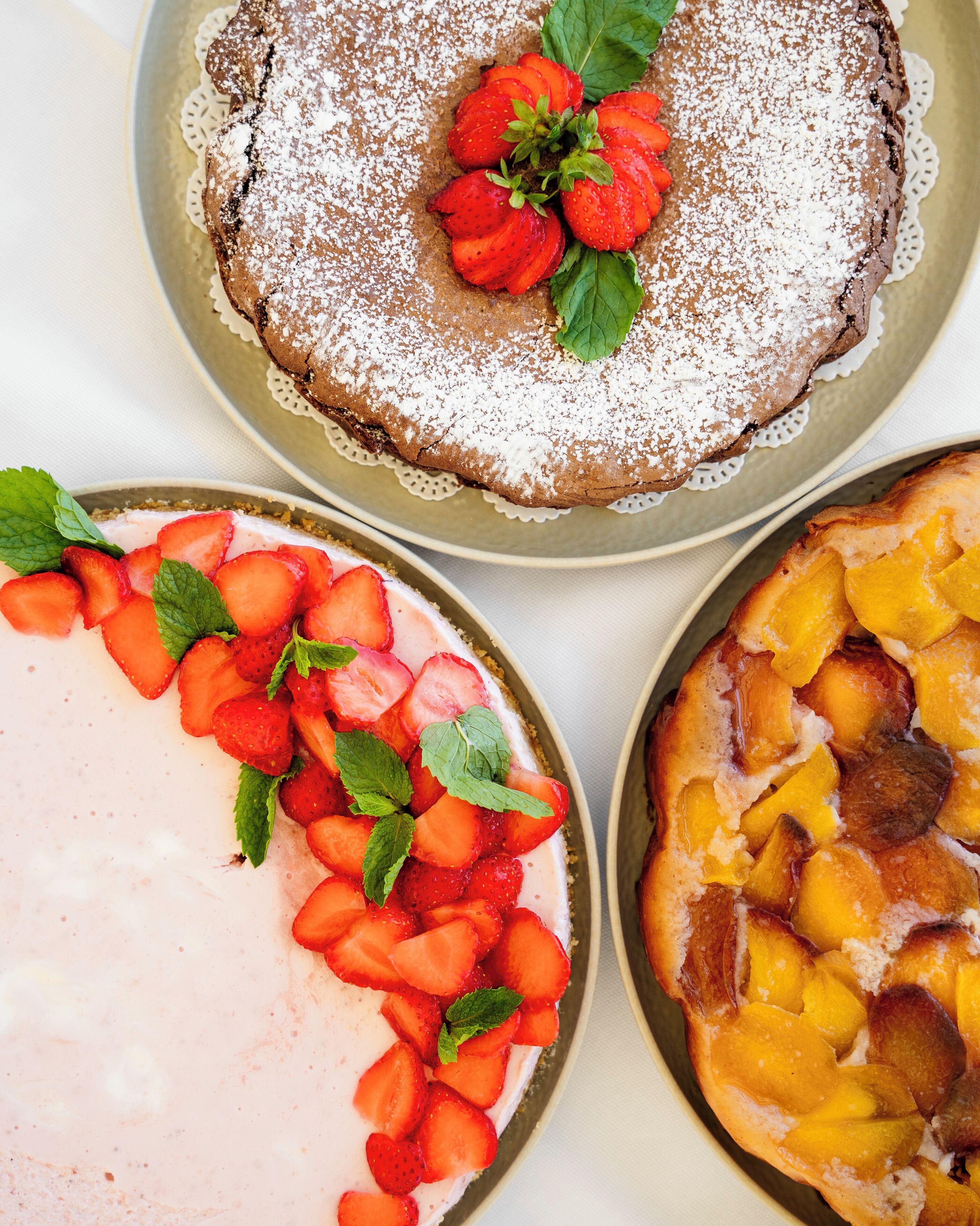 Three desserts: a chocolate cake with strawberries, a strawberry dessert with mint, and a peach dessert.