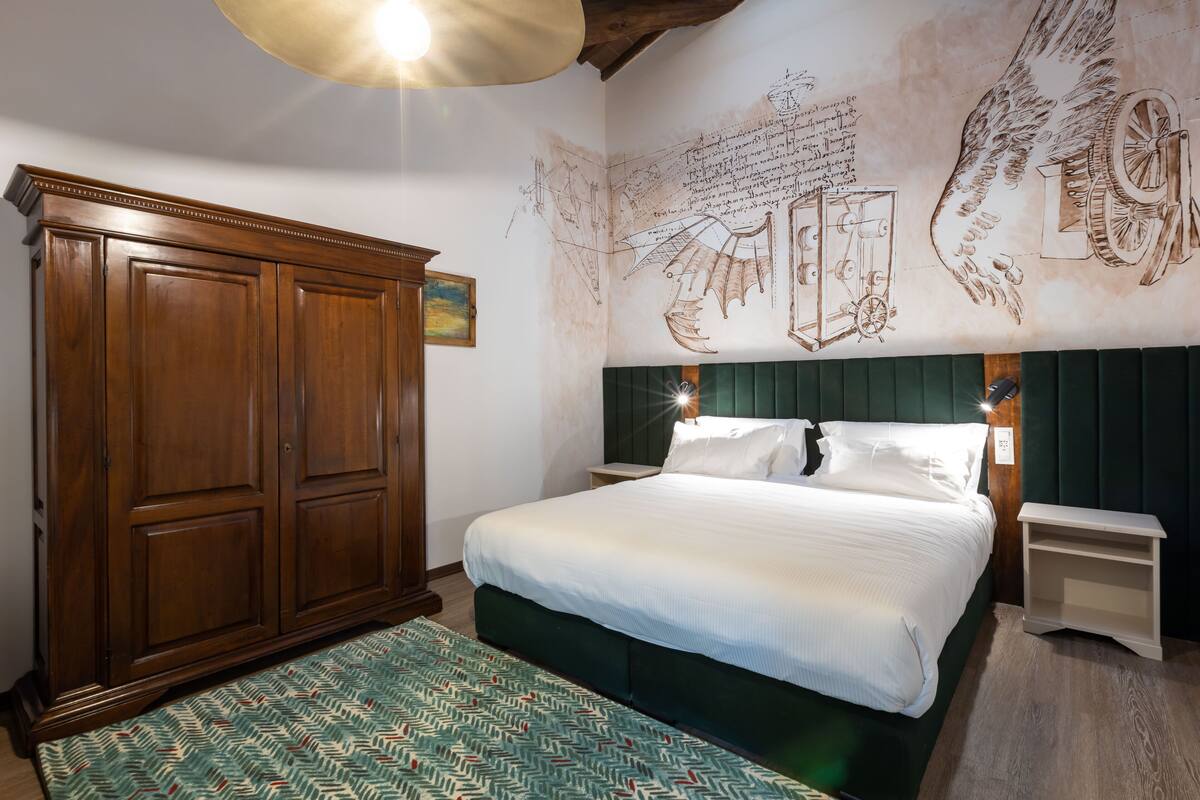A bedroom with a large wooden wardrobe, a green upholstered headboard, and a patterned rug.