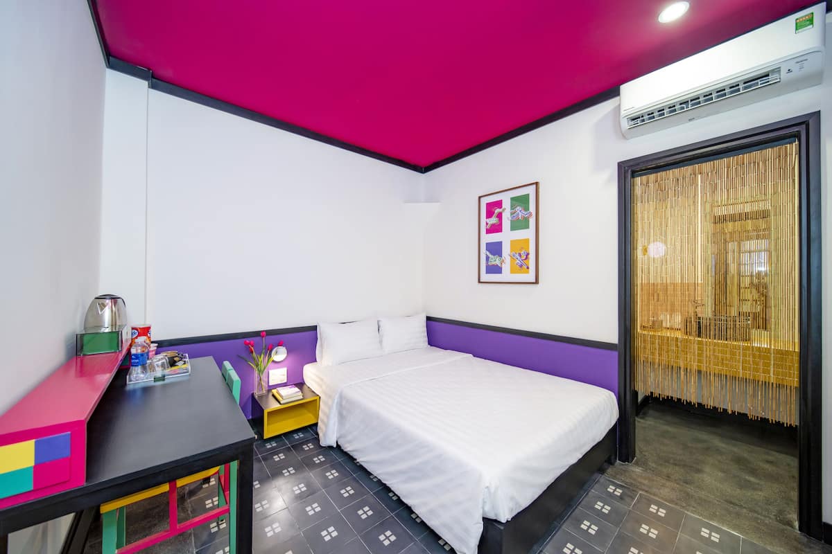 Habitación de hotel con cama, escritorio, mesita de noche, lámpara y ventana con cortinas.