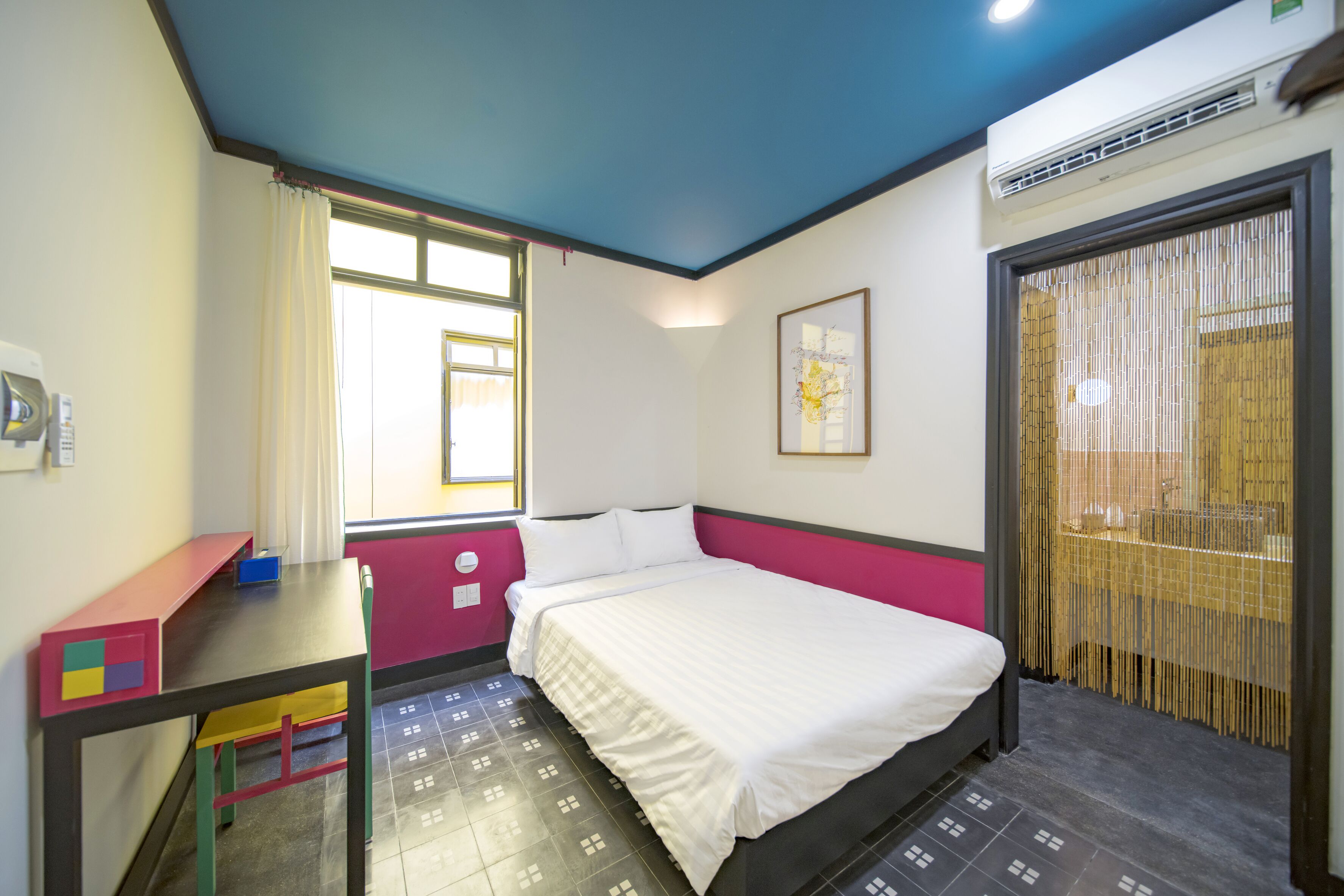Una habitación con cama, escritorio, silla, ventana con cortinas y aire acondicionado de pared.