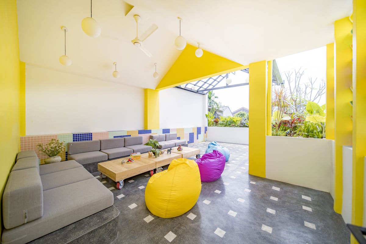 Un espacio exterior luminoso y moderno con un sofá gris, un sillón inflable amarillo y una mesa de centro de madera.
