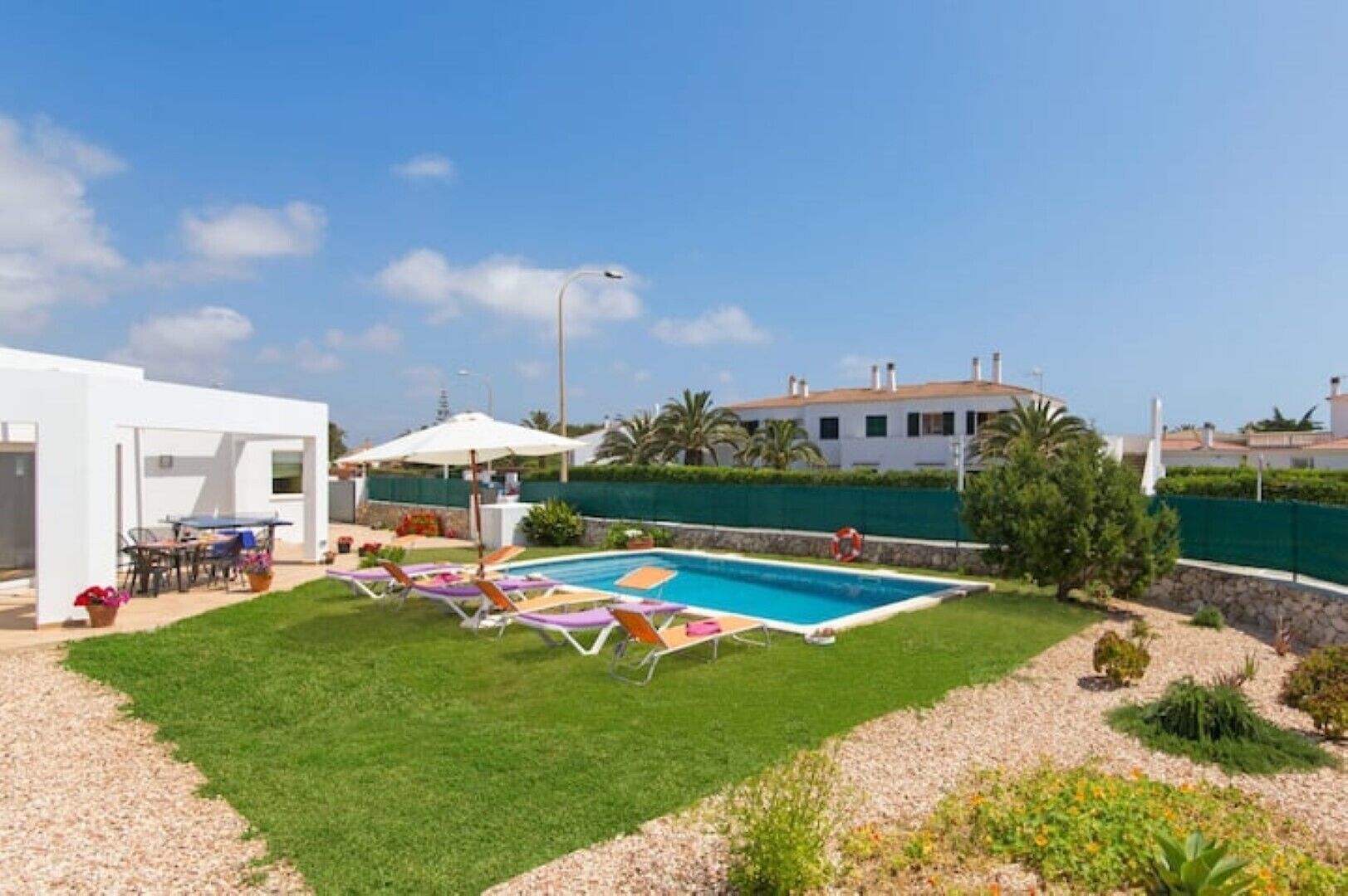 A backyard with a swimming pool, lounge chairs, a barbecue area, and a white building.
