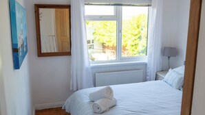 A bedroom with a wooden floor, a bed with white bedding, a window with curtains, a bedside table with a lamp, and a mirror on the wall. - Pet friendly, comfortable family home with sea views near the Giant's Causeway (Bushmills)