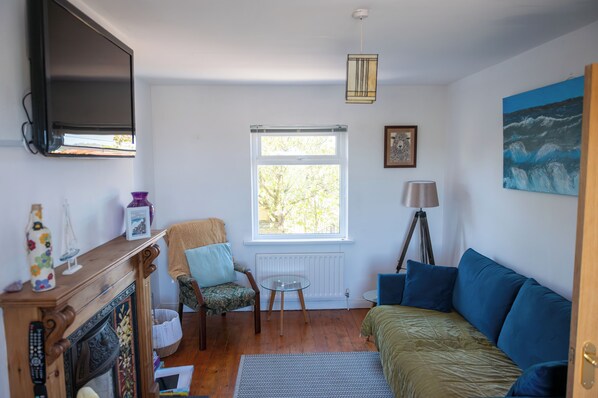 Ein Zimmer mit Kamin, einer Couch, einem Sessel, einem Tisch, einer Lampe und einem Gemälde an der Wand.