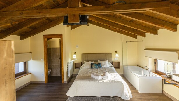 Een slaapkamer met een groot bed, een vrijstaand bad, houten balken in het plafond en een raam.