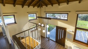 Een modern interieur met een houten plafond, grote ramen, een trap en hangende hanglampen.