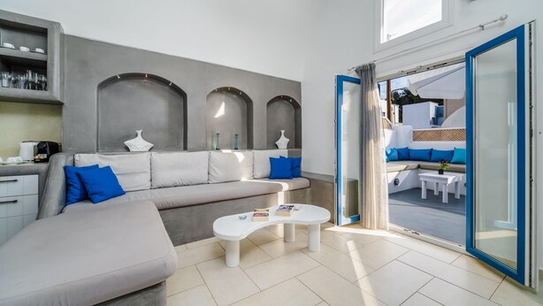 A modern living room with a grey sofa, a white coffee table, and a view of the outdoor seating area through a glass door. - Casa Maritina Private Villa With Jacuzzi (Santorini)