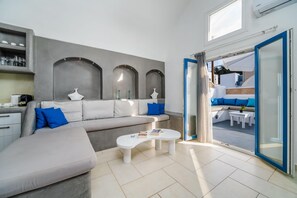 A modern living room with a grey sofa, a white coffee table, and a view of the outdoor seating area through a glass door.