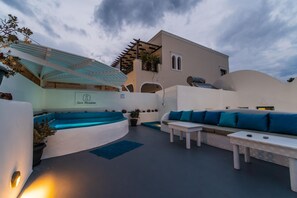 A modern outdoor seating area with a pool, a white building with a sign reading "Casa Maritino," and a clear sky.