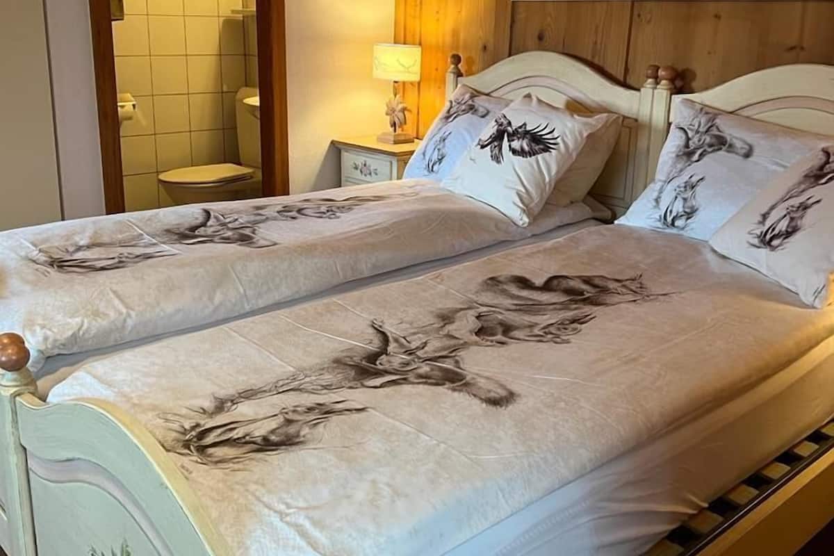 A double bed with floral bedding, a wooden headboard, a nightstand with a lamp, and a bathroom visible through an open door.