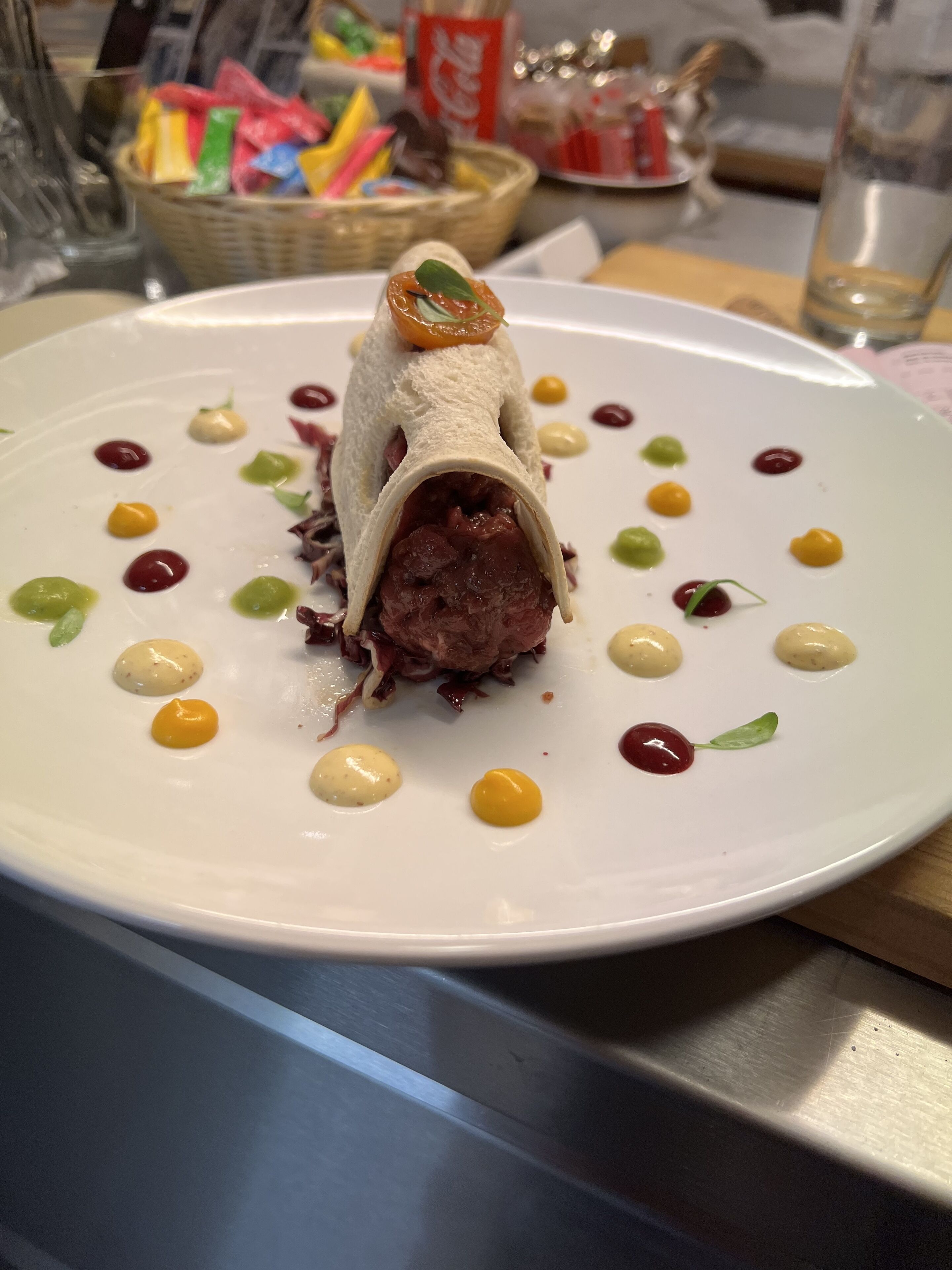 Ein Teller mit Essen, im Mittelpunkt ein Fleischröllchen, umgeben von kleinen Soßenklecksen und Garnituren.