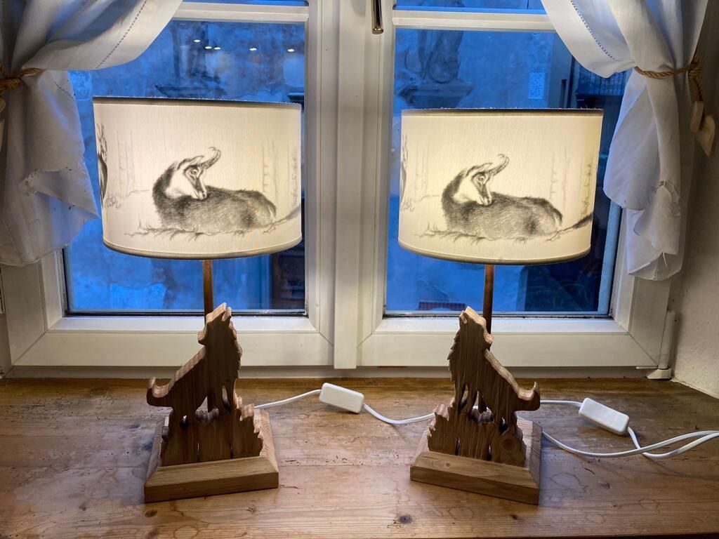 Dos lámparas de madera con diseños de animales sobre una mesa de madera junto a una ventana con cortinas.