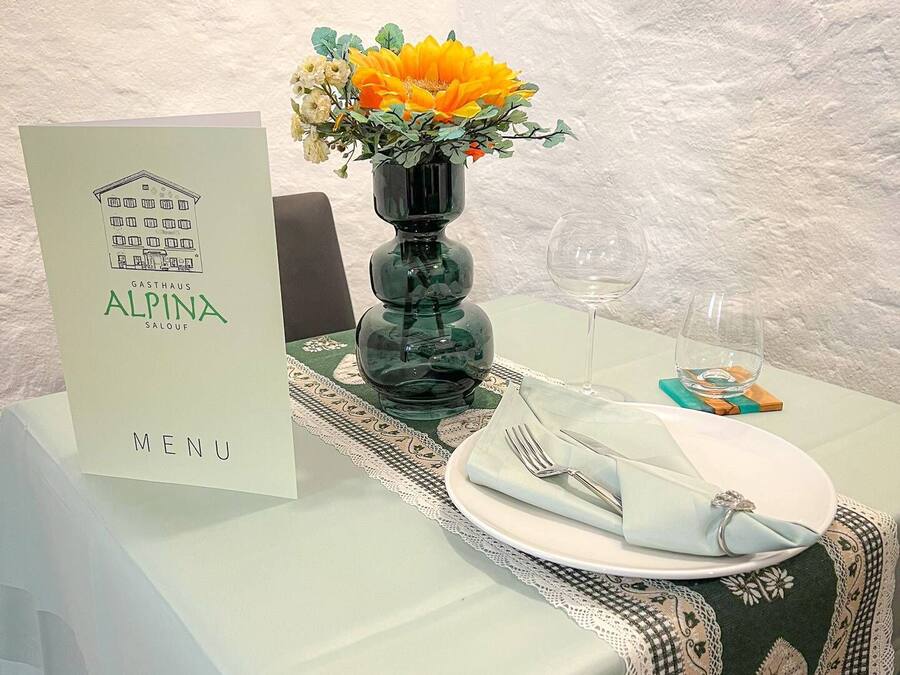 A table set with a menu, a vase with flowers, and a glass of water.